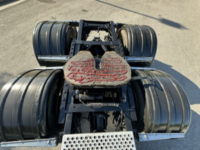 Kenworth T880 tractor chassis showing rear dual rear axles and fifth wheel, with black fuel tanks and metal steps visible.