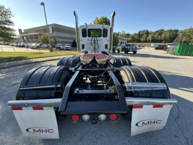 Kenworth T880 rear view showing fifth wheel, dual rear axles, mud flaps with MHC logo, and white cab in distance.