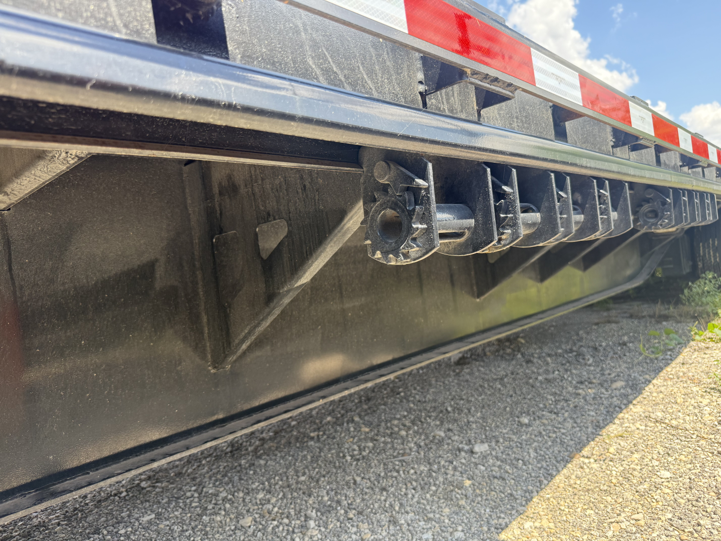Trailer underside showing lower deck and pocketed tie-downs on a steel drop deck trailer.