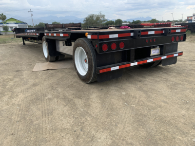 Flatbed trailer with Iron Lite spread axle drop deck showing rear and left side, black frame, white wheels, red/white reflective markings.