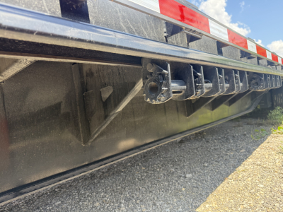 Trailer underside showing lower deck and pocketed tie-downs on a steel drop deck trailer.
