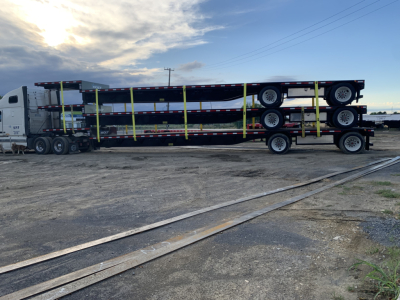 Trailer showing stacked Iron Lite spread axle steel drop deck semi-trailer with three-axle configuration and bright yellow straps securing bunks.