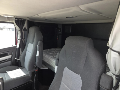 Kenworth W990 sleeper cab interior showing driver seat and bunk area with gray fabric seats and overhead cab, dashboard not visible.