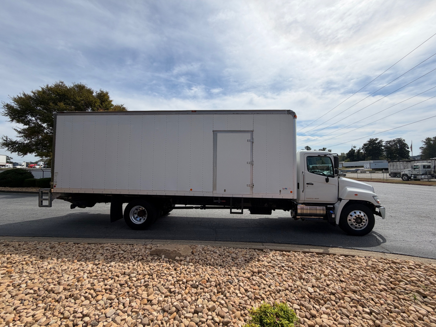 Truck side view showing a 2019 Hino 268A box truck with a large rectangular cargo box and cab, VIN 5PVNJ8JV2K4S71438 on a lot.