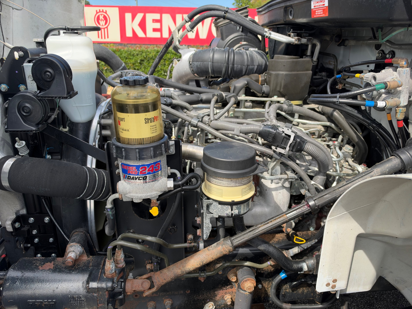 Engine bay of a 2019 Hino 268A showing brake fluid reservoir, fuel filter canister, hoses, and metal engine components.