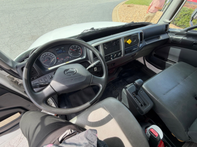 Cab interior of a 2019 Hino 268A box truck showing steering wheel, dashboard, and gear selector with the instrument cluster and center console.