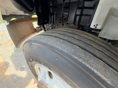 Front wheel and suspension area of a 2019 Hino 268A box truck showing a dual rear axle wheel and tire, partial cab interior components, and wheel well.
