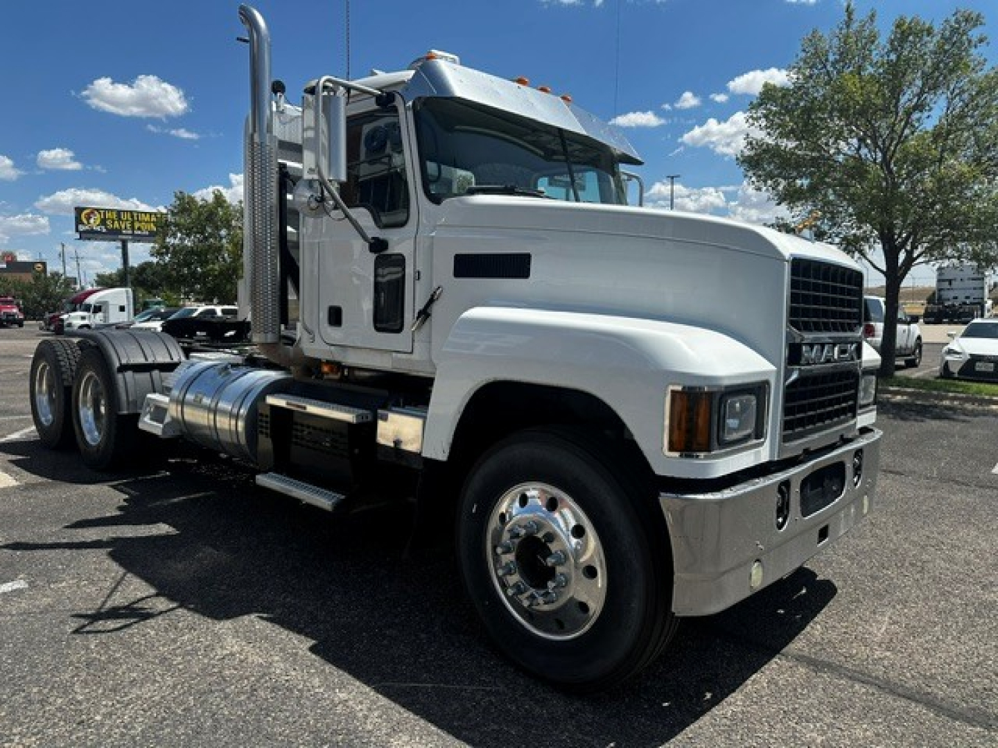 Mack PI64T conventional daycab truck in a parking lot, side view showing chrome fuel tanks, step, and dual rear axles.