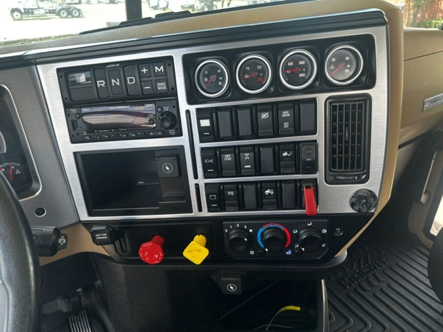 Dashboard of a 2022 Mack PI64T daycab showing gauge cluster, steering wheel, control switches, and gear selector with red and yellow knobs.