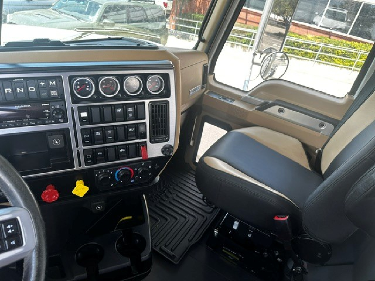 Mack PI64T cab interior showing steering wheel, dashboard with gauges, gear selector, and black floor mats.