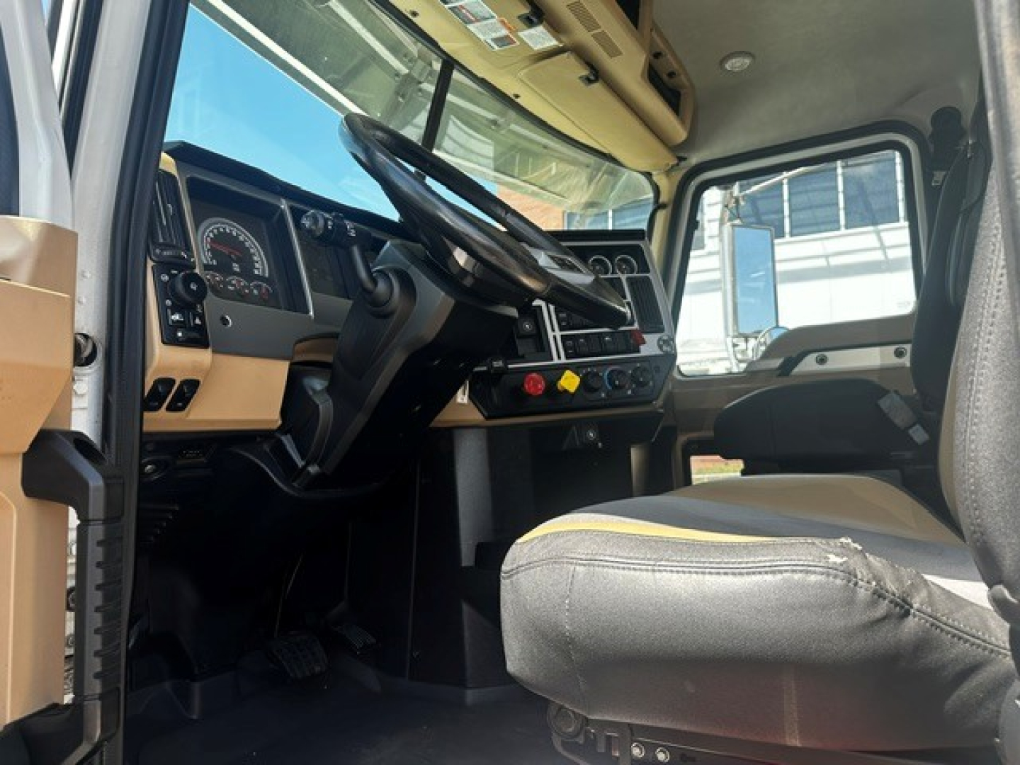 Mack PI64T cab interior showing steering wheel, dashboard gauges, and driver seat with beige and black upholstery.
