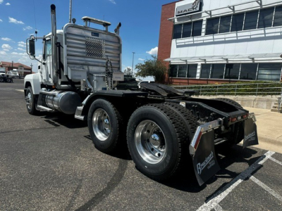 Truck chassis of a 2022 Mack PI64T daycab, rear view showing dual rear axles, heavy-duty tires, chrome exhaust stacks, and a chrome fuel tank with a white cab in the background.