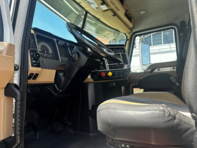 Mack PI64T cab interior showing steering wheel, dashboard gauges, and driver seat with beige and black upholstery.