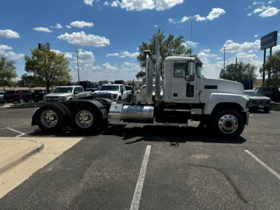 Truck side view showing 2022 Mack PI64T conventional daycab with dual rear axles and sleeper cab, white cab, chrome fuel tanks, and chrome exhaust stacks.