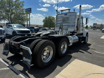 Truck rear view showing dual rear axles and fifth-wheel on a Mack PI64T conventional cab. Chrome fuel tanks, aluminum cab, mud flaps, and hanging chain visible.