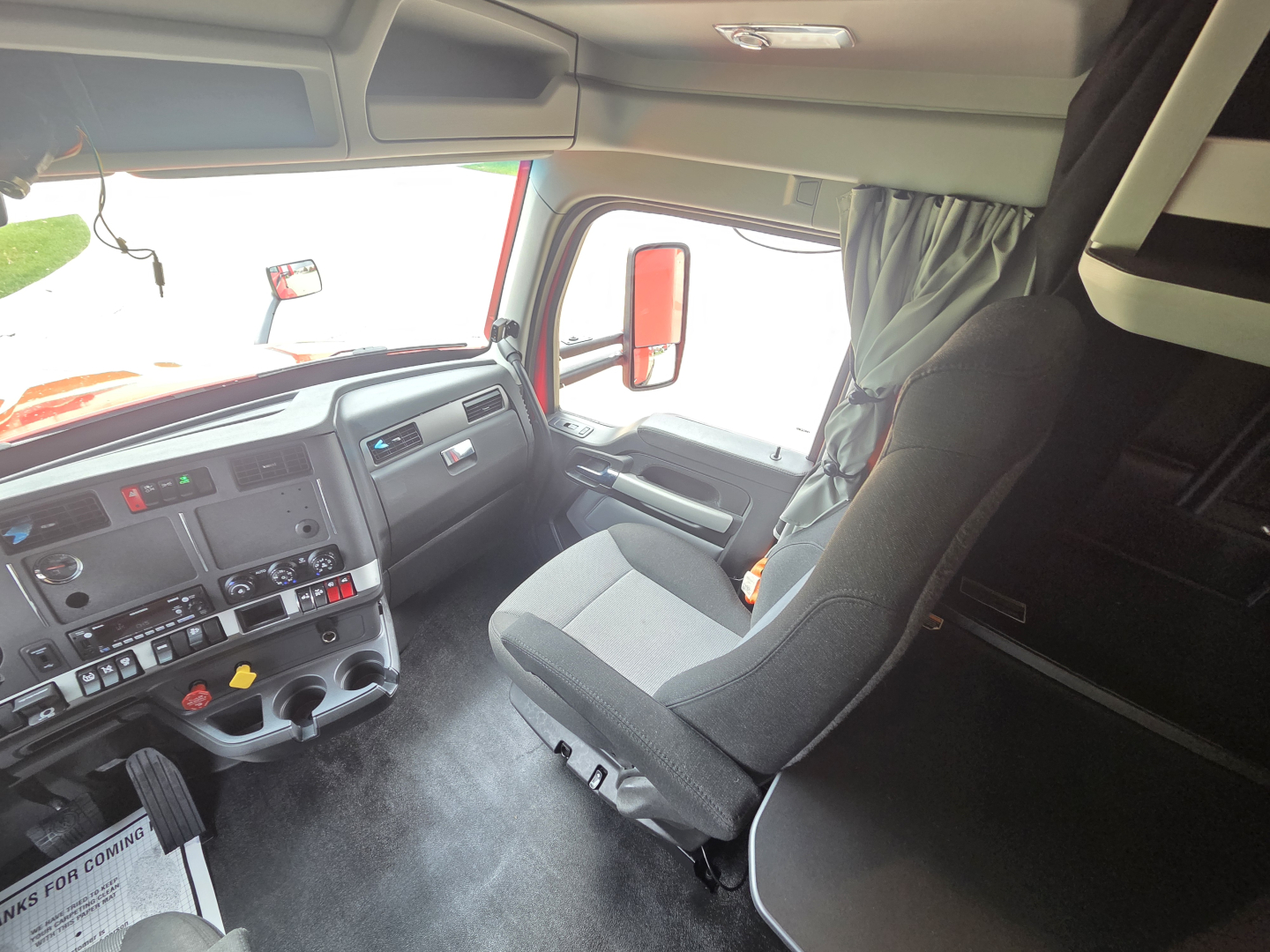Truck cab interior showing dashboard with controls and steering wheel; passenger seat; day lighting through window.