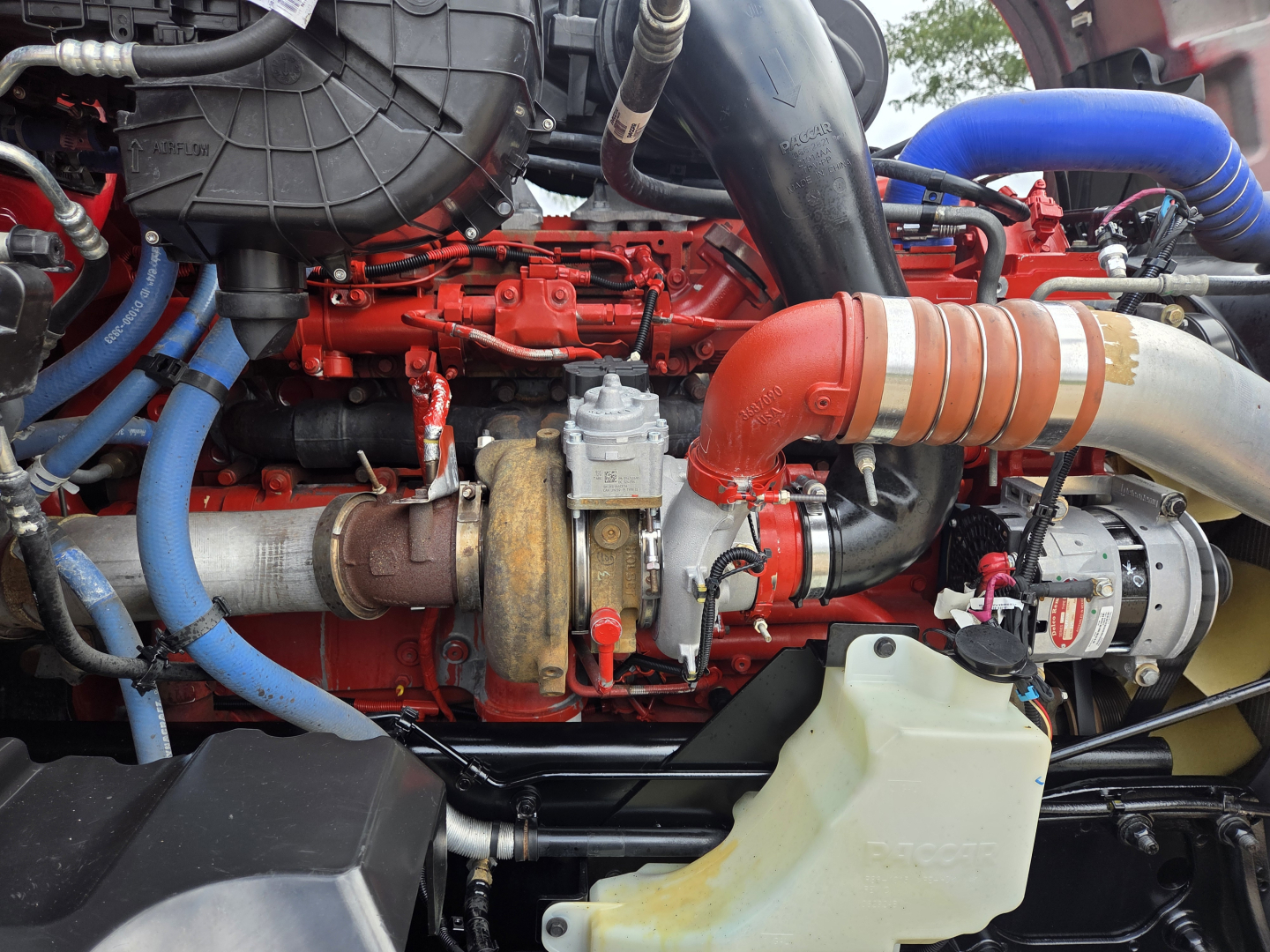 Kenworth T680 engine bay with red engine block, blue hoses, and large red turbocharger pipe visible.