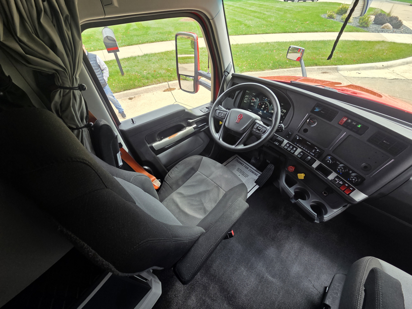 Kenworth T680 interior view showing steering wheel, dashboard and driver seat with controls and center console.