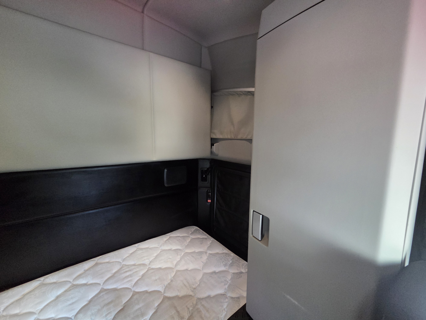 Kenworth T680 sleeper cab interior showing bed area and partition with light-colored upholstery.