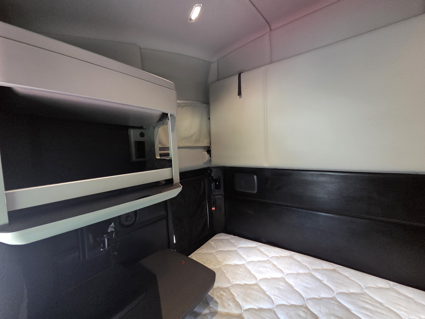 Kenworth T680 sleeper cab interior showing bunk area with quilted mattress and overhead storage shelf.