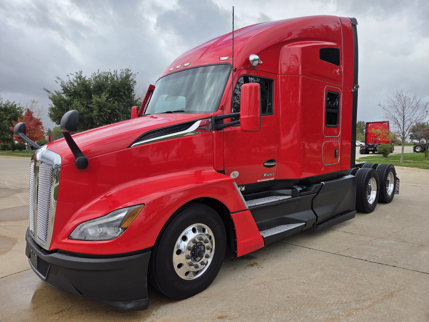 Kenworth T680 sleeper cab truck in red, side view showing front bumper, hood, windshield, mirrors, and dual rear axles.