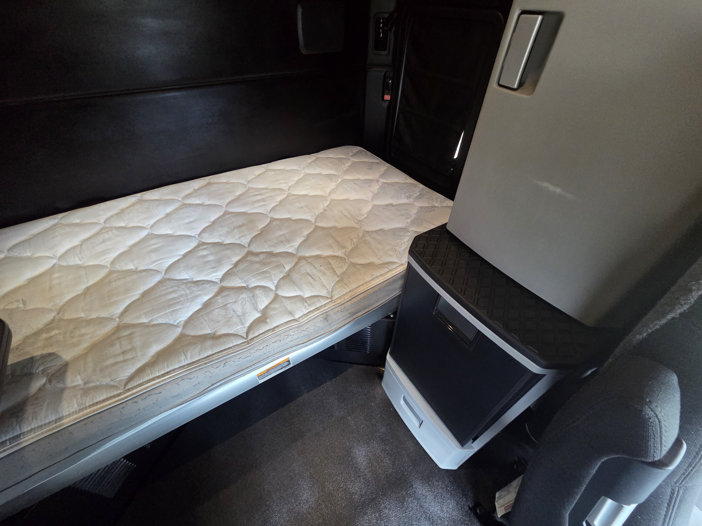 Kenworth T680 sleeper cab interior showing single bed with quilted mattress and small cabinet fittings.
