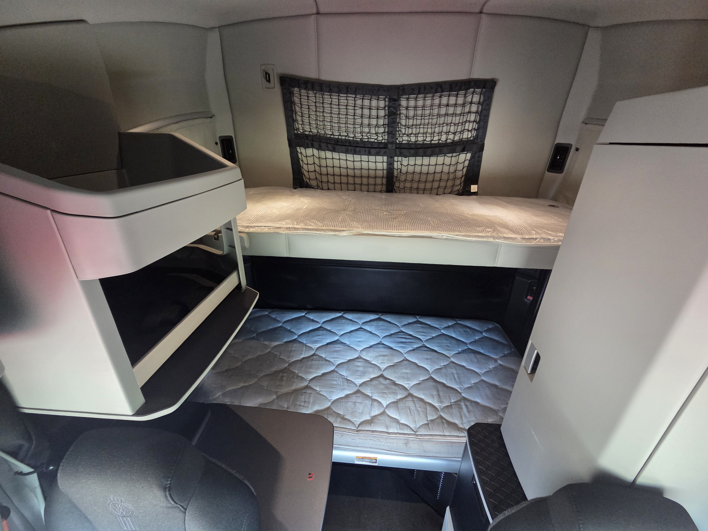 Kenworth T680 sleeper cab interior showing bunk bed and storage shelves with quilted mattress on lower bed.