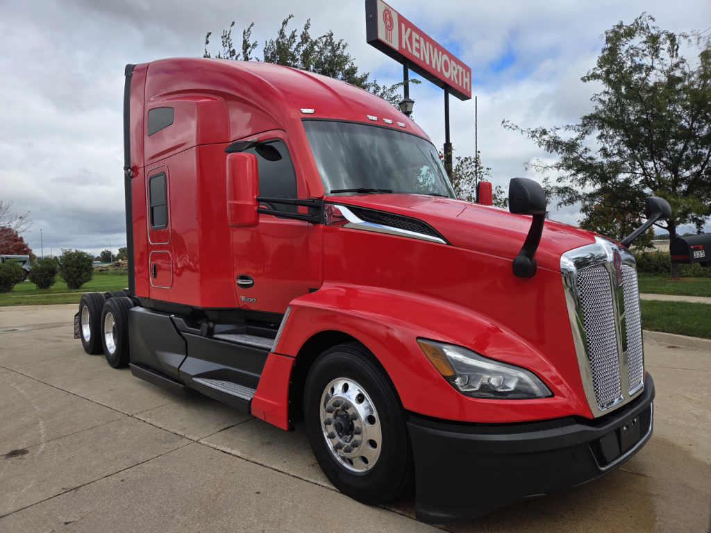Kenworth T680 sleeper cab semi-truck in red with chrome grille and black bumper, parked outside dealership.
