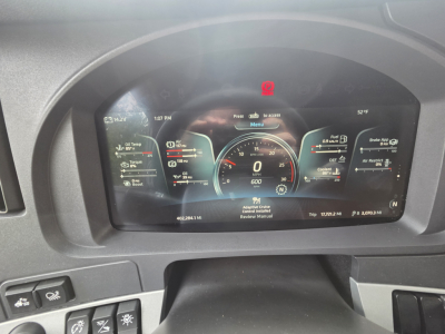 Dashboard display of a Kenworth truck showing digital gauges and warning icons. Speedometer reads 0, odometer 0, center RPM gauge, left displays oil temp and other vehicle status, right shows fuel and range.