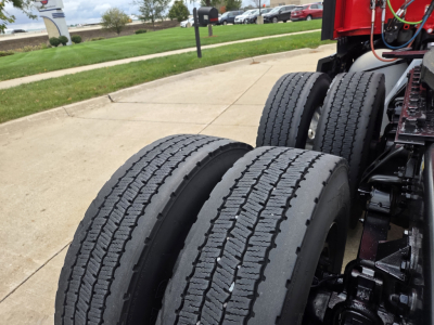 Kenworth T680 wheel area showing dual rear axles and tires with visible tread and suspension components.