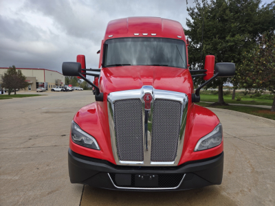 Kenworth T680 2023 front view showing bold chrome grille and red hood, dual large side mirrors, black bumper, daytime running lights.