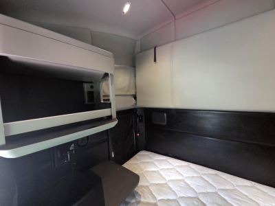 Kenworth T680 sleeper cab interior showing bunk area with quilted mattress and overhead storage shelf.