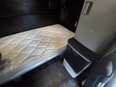 Kenworth T680 sleeper cab interior showing single bed with quilted mattress and small cabinet fittings.