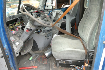 Truck cab interior showing steering wheel, dashboard wires, exposed wiring, and a worn seat with seat belt.