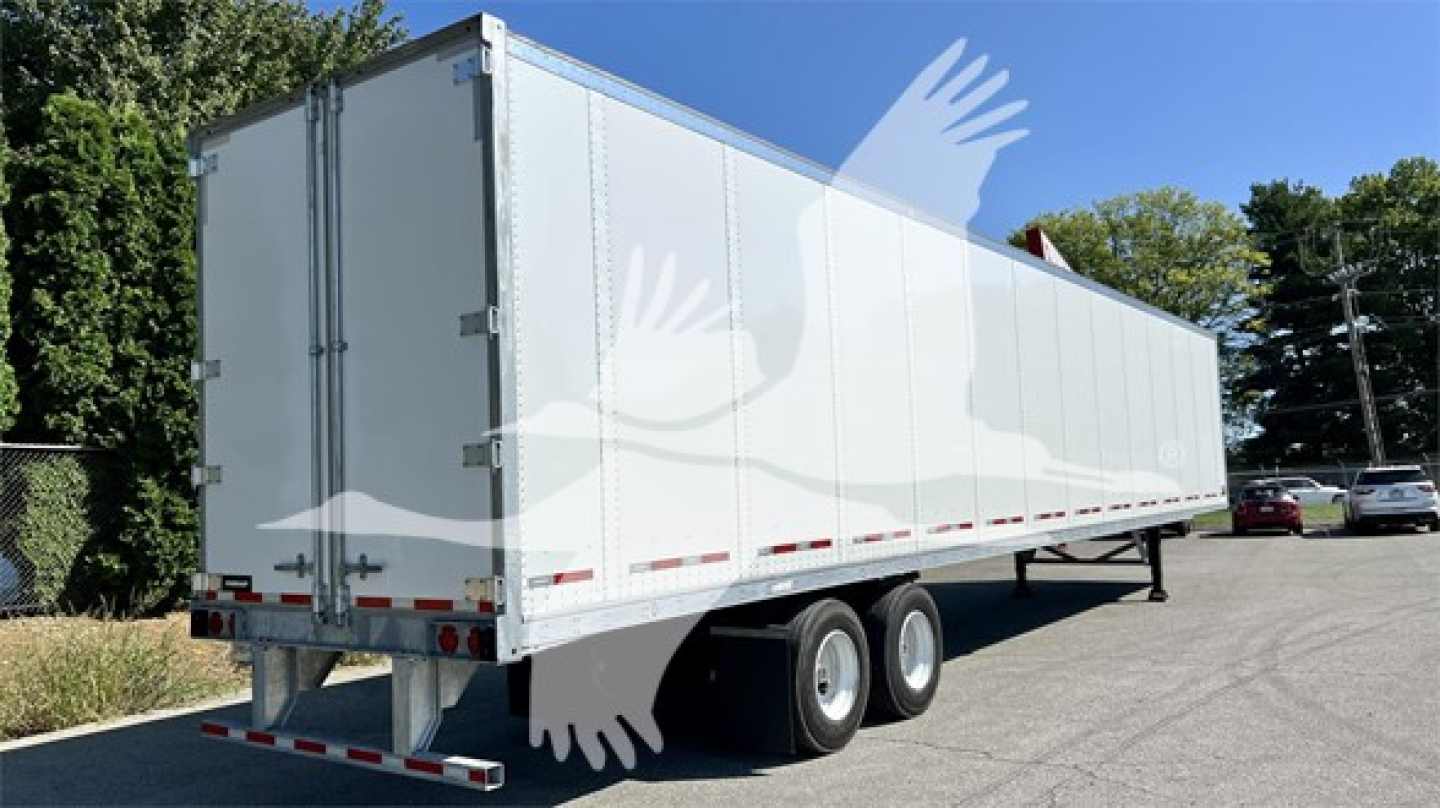 Trailer side and rear showing a white Fruehauf plate van with dual rear doors and support legs, no visible branding on the body; standard trailer features visible.