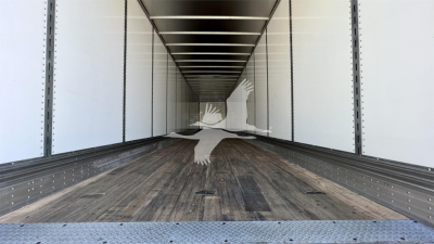 Interior of a Fruehauf van trailer cargo area with wooden floor, white side walls, steel ribs, and rear access at the far end.