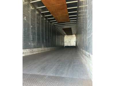 Trailer interior showing empty cargo space with metal sidewalls and a wooden ceiling beam, long perspective toward rear door.