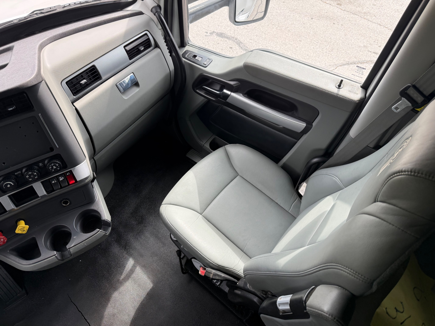 Truck cab interior from driver's side showing light gray leather seat, dashboard with controls, center console, and door panel.