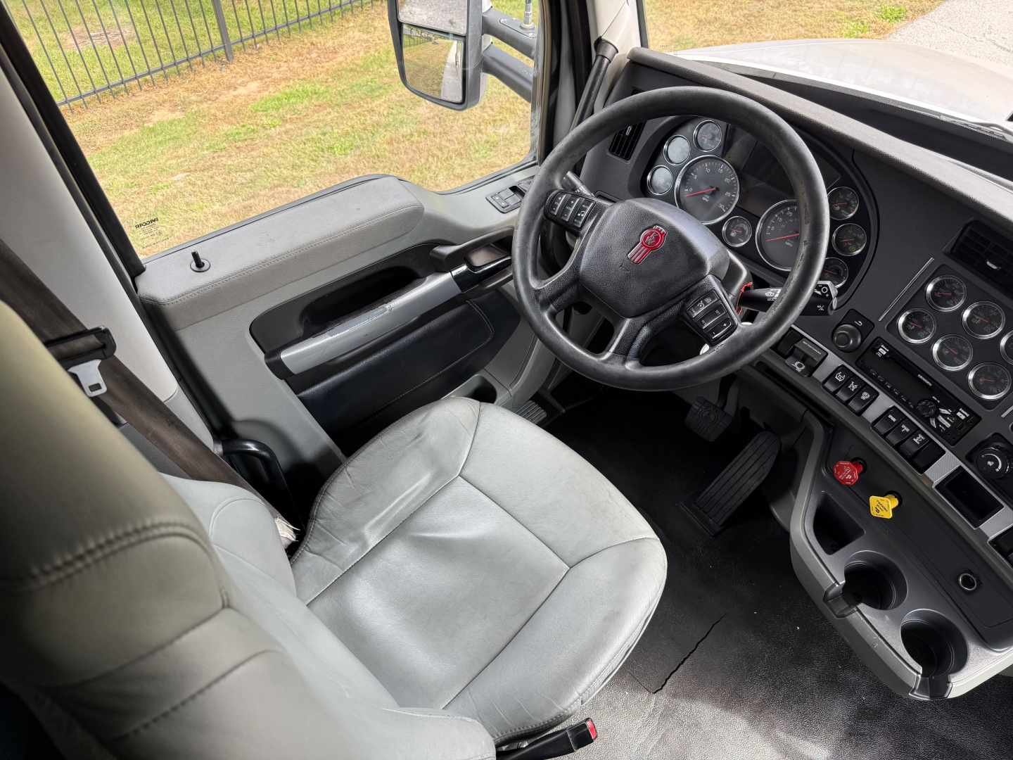 Kenworth T680 cabin interior showing steering wheel with red logo, dashboard gauges, and driver seat area.