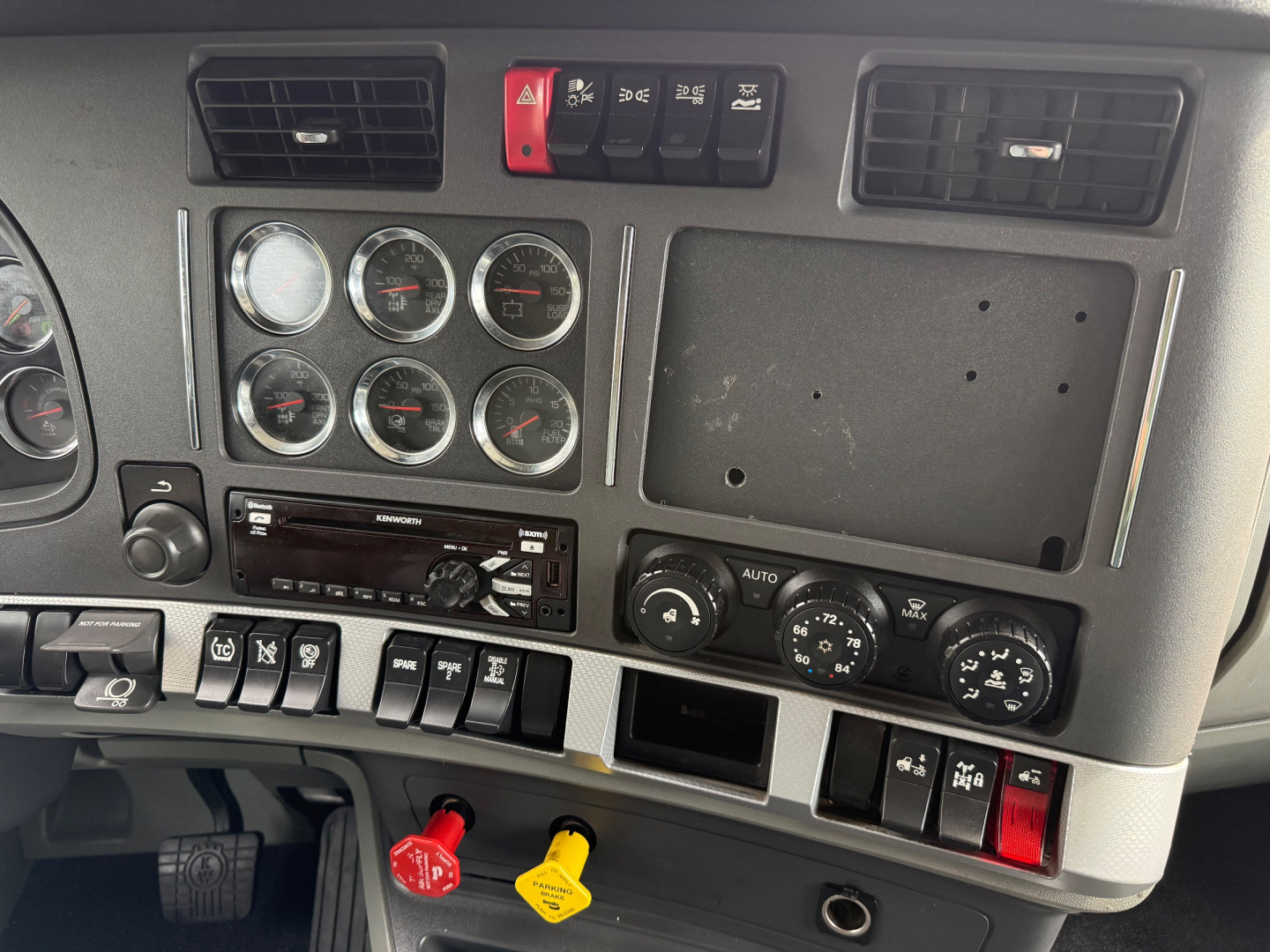 Kenworth T680 dash panel showing multiple gauges, switches, and climate controls; red and yellow knobs visible, blank slot for radio, various switch labels.