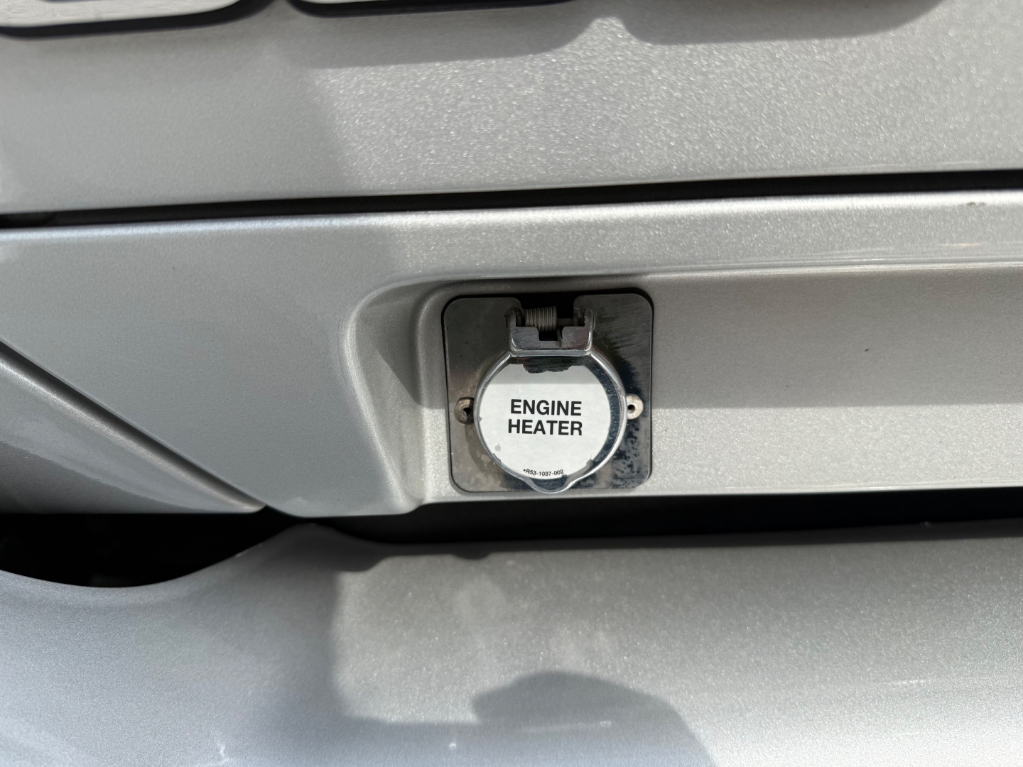 Close-up of Kenworth T680 front showing a circular engine heater cap labeled 'ENGINE HEATER' on a metallic grille area.