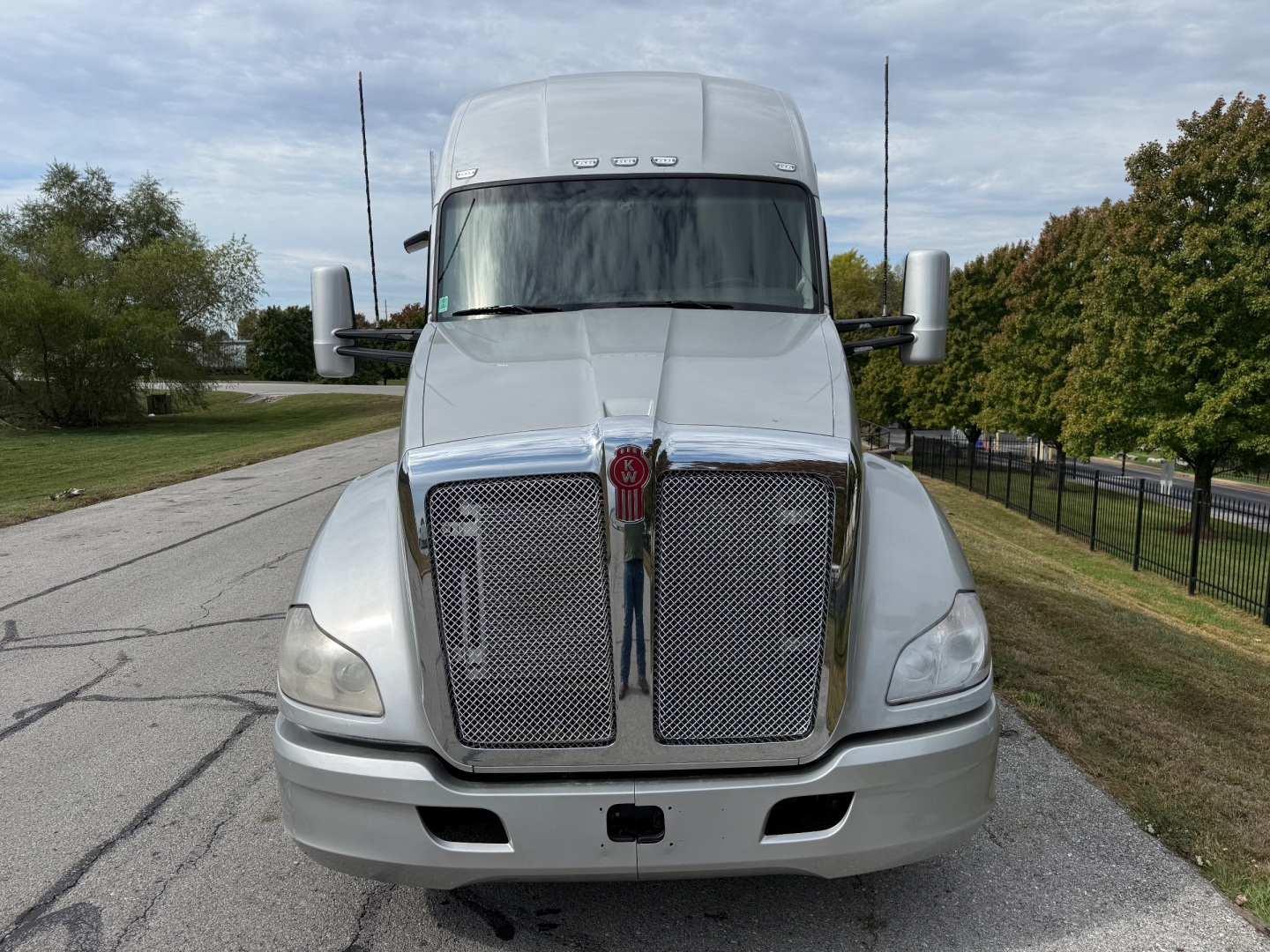 Kenworth T680 front view showing chrome grille and bumper, white exterior, side mirrors, and highway in background.