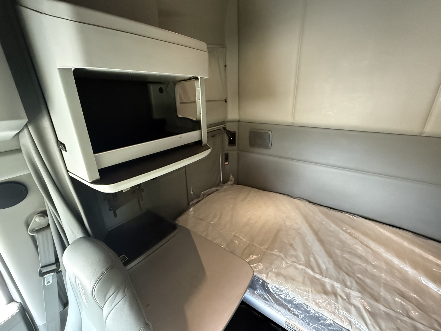 Kenworth truck sleeper cab interior showing bunk area with mattress and overhead storage shelf.