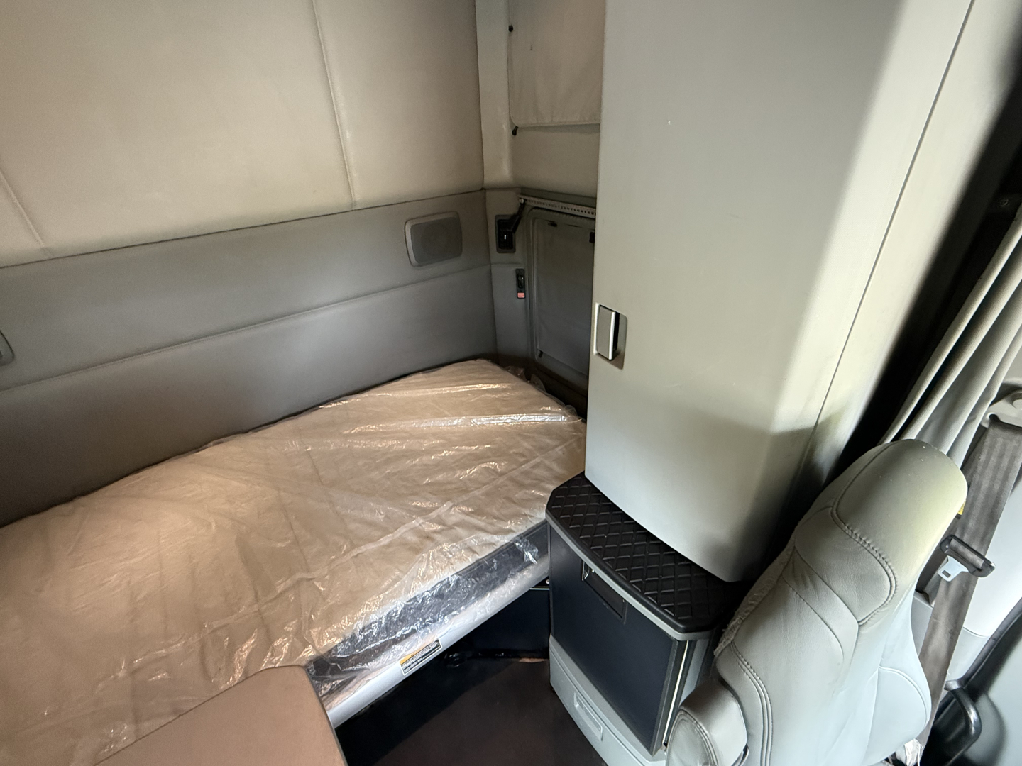 Kenworth T680 sleeper cab interior bed area with light-colored upholstery and storage cabinet.