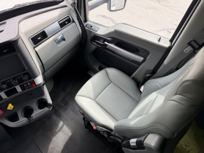 Truck cab interior from driver's side showing light gray leather seat, dashboard with controls, center console, and door panel.