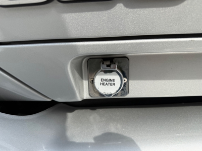 Close-up of Kenworth T680 front showing a circular engine heater cap labeled 'ENGINE HEATER' on a metallic grille area.