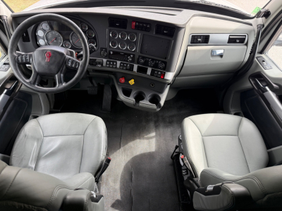 Kenworth T680 truck interior driver seat and dashboard with steering wheel, gauges, and center console; grayscale seats and pedals visible.