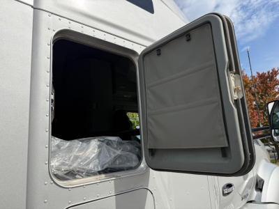 Kenworth T680 cab door open showing side window and sleeper area with plastic-wrapped seat visible.