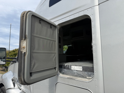 Kenworth T680 sleeper cab with side door open showing interior cargo space and windowed sleeper area.
