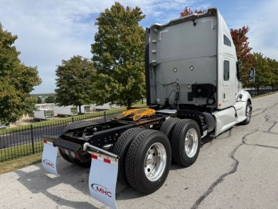Kenworth T680 tractor rear view showing fifth wheel and dual rear axles with tires, sleeper cab, white paint, side mirrors, parking lot.